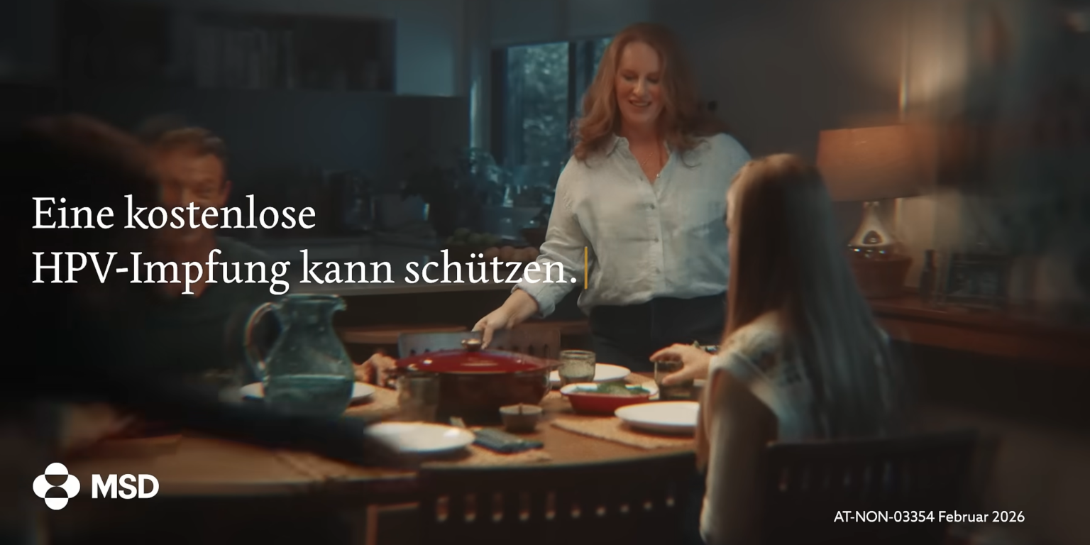 Familie sitzt beim Abendessen an einem Esstisch, im Hintergrund warmes Licht und eine Frau spricht freundlich mit Kindern.